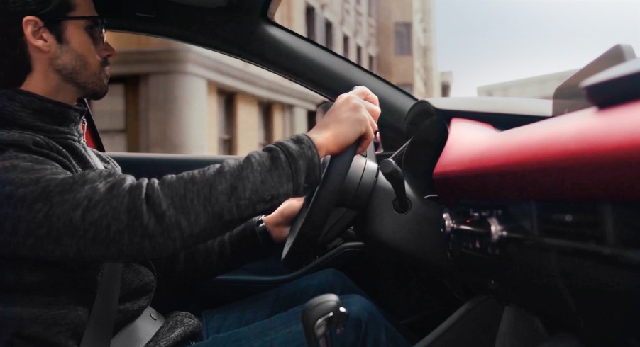 Man holding the steering wheel of a Mazda 3 sports sedan with a red interior