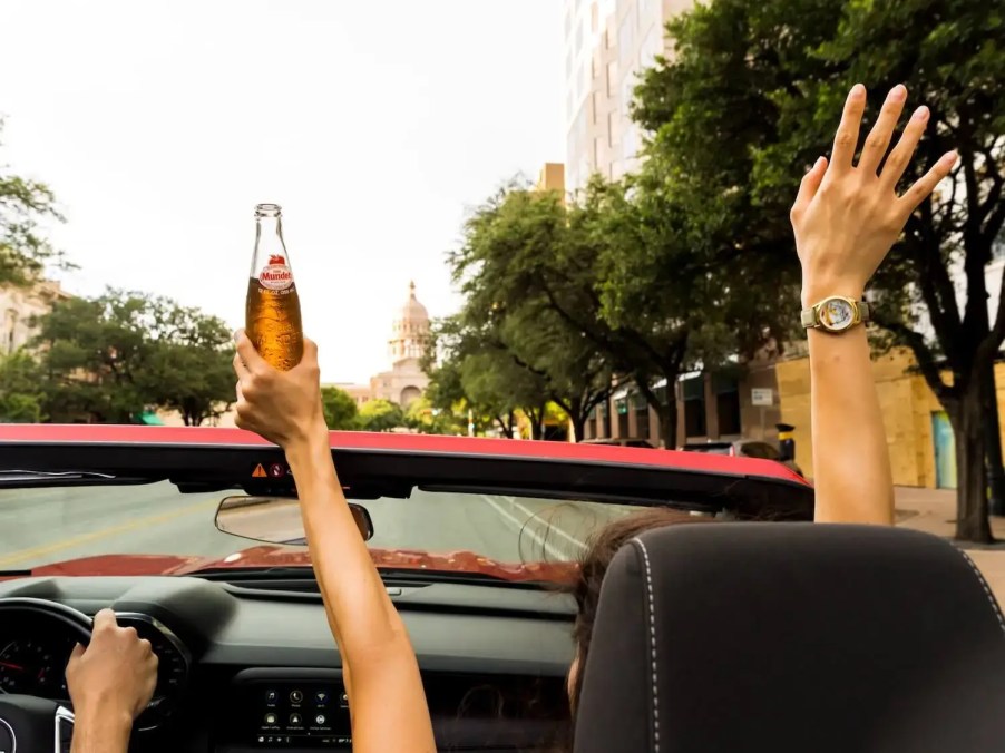 Passengers drinking in a convertible car.