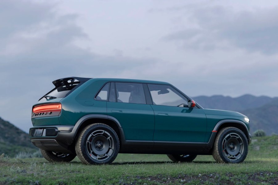 Blue Rivian crossover EV concept car parked in a field, a cloudy sky visible in the background.