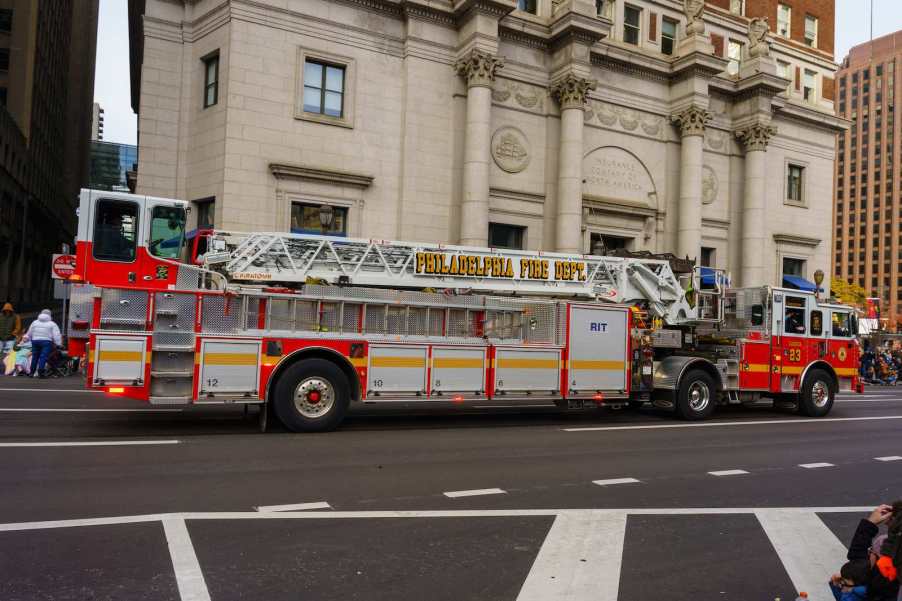 Red fire truck with a tiny cab at the back driving through a Philadelphia parade.