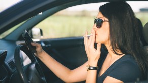 Woman smokes a cigarette while driving a car.