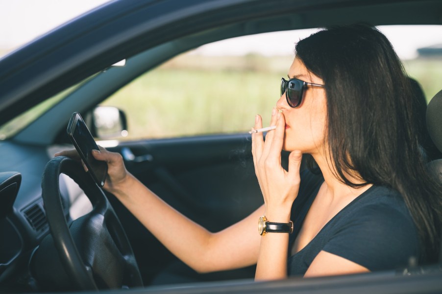 Woman smokes a cigarette while driving a car.