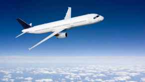 An airplane painted white flying against a blue sky tilted in right profile view clouds below