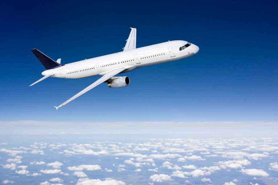 An airplane painted white flying against a blue sky tilted in right profile view clouds below