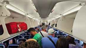 Airplane interior view of passengers deplaning with luggage compartments open people standing in aisle