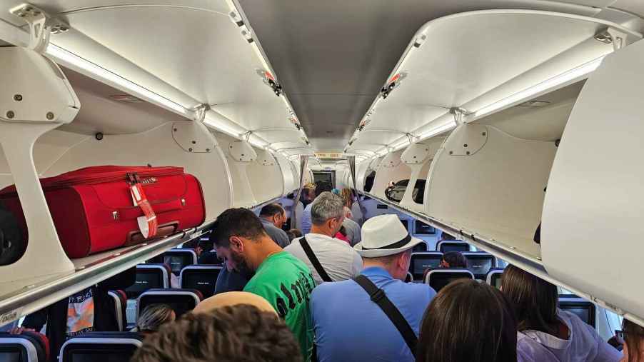 Airplane interior view of passengers deplaning with luggage compartments open people standing in aisle