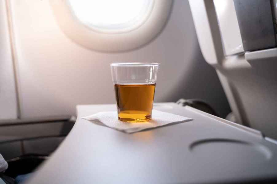 A cup of alcohol that appears to be neat whiskey on a napkin on a plane tray table