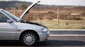 A silver car parked in right mid-profile view with hood propped open in remote area