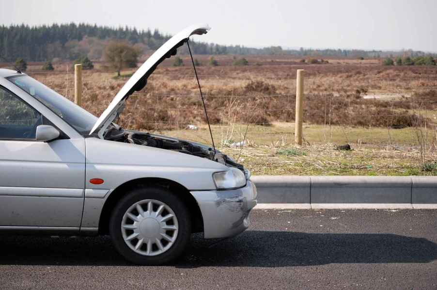 A silver car parked in right mid-profile view with hood propped open in remote area