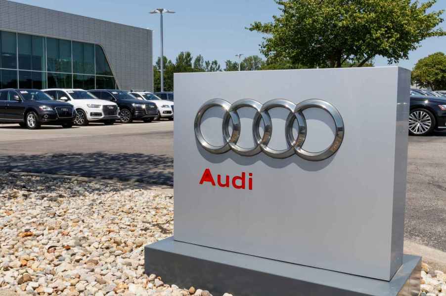 The exterior sign of an Audi dealership with Audi vehicles parked in a row behind