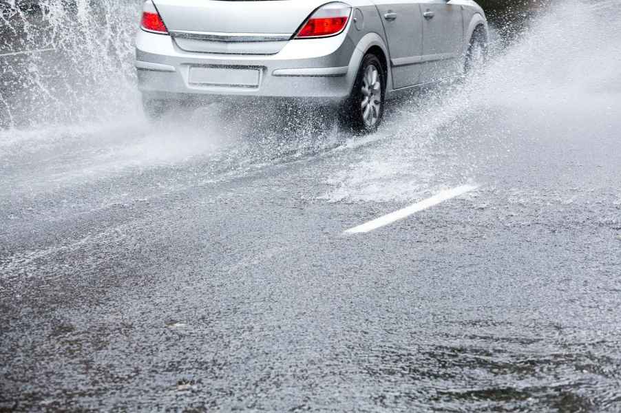 A silver car drives through heavy water on road risk of aquaplaning