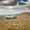 A light-colored Jaguar I-Pace electric SUV driving up a grassy hill remote location