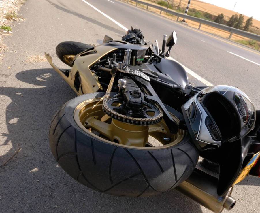 A motorcycle rider takes a picture of their bike after a crash on a two-lane highway.