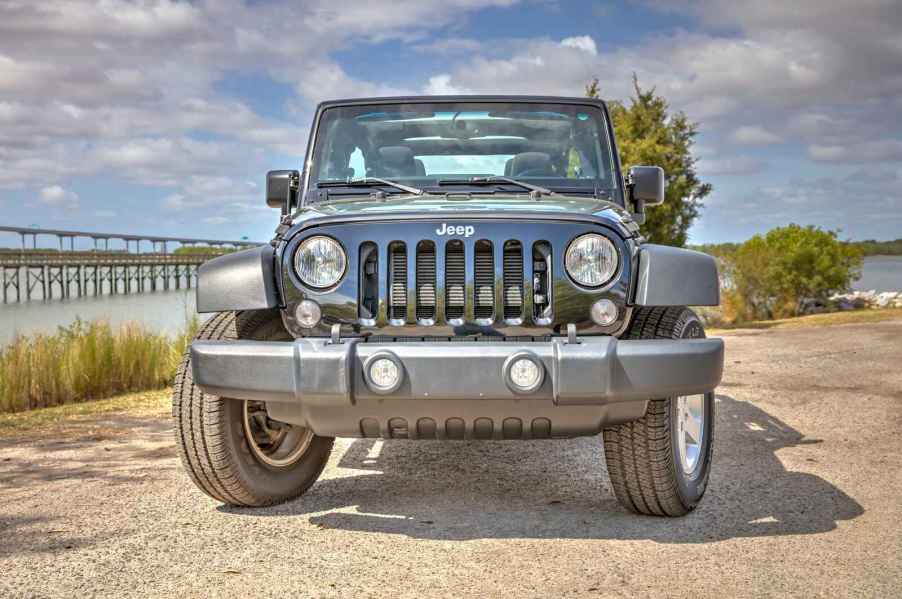 A black Jeep Wrangler parked near water with bridge in background in direct front view with front tires turned to left frame