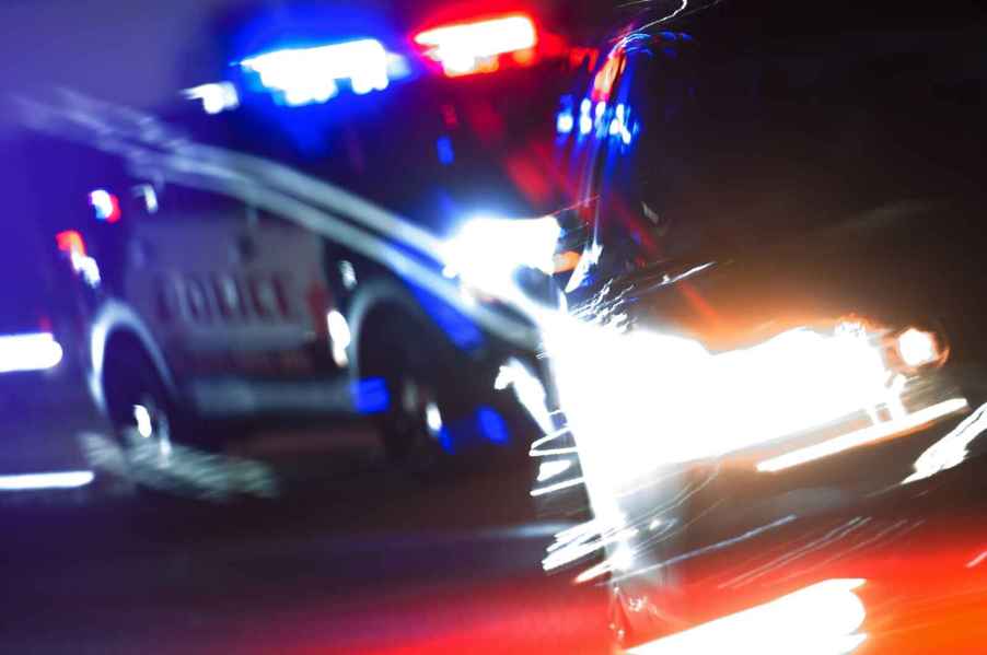 A blurred night scene of a police car with lights on and another car in front of it, illustration of how a Tesla driver using FSD mode ran into a police car in CA on June 14, 2024.