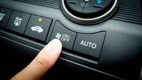 A finger getting ready to push AC on/off button in car with recirculate button on