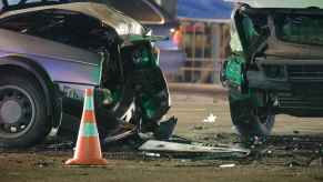 A close view of two vehicles with damaged front ends after a collision with an orange cone in foreground