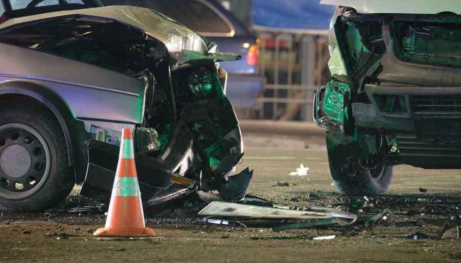 A close view of two vehicles with damaged front ends after a collision with an orange cone in foreground