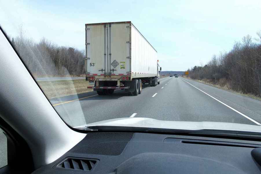 The right rear view of a semi-truck from the left front corner of the dash of a car on a highway