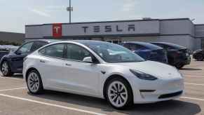 A white Tesla Model 3 EV sedan parked at a Tesla dealership parking lot spot in right front angle view