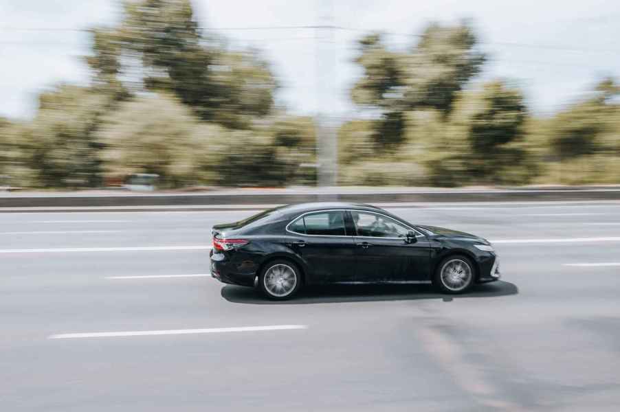 A black Toyota Camry sedan driving fast on a highway