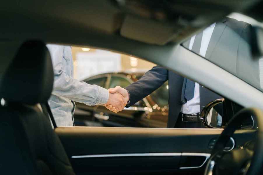 Two men shaking hands view from inside car interior at a dealership