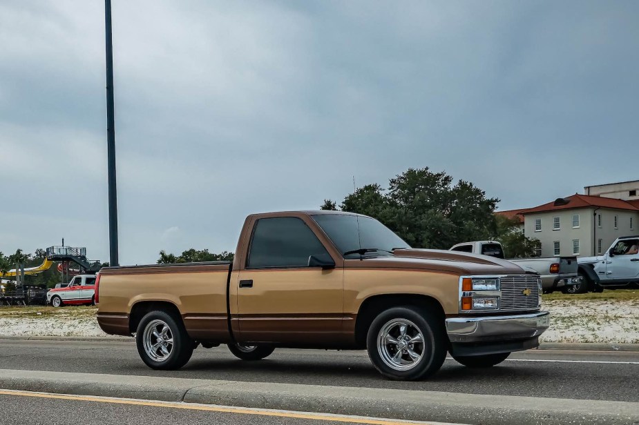 A 1990s, Chevrolet GMT400 classic pickup truck drives down the road in front of a car show.