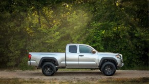 A silver 2019 Toyota Tacoma parked in the woods on a gravel road in full right profile view these trucks hold their resale value best according to sources