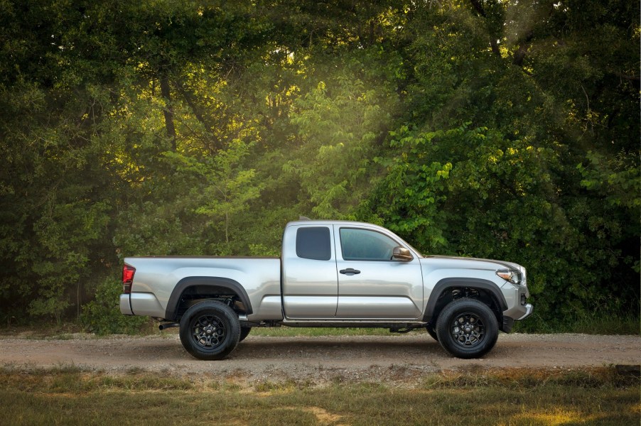 A silver 2019 Toyota Tacoma parked in the woods on a gravel road in full right profile view these trucks hold their resale value best according to sources