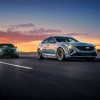 Two Cadillac sedans drive on a race track, the sunset behind them.