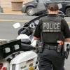 A police officer walks up to their motorcycle in body armor.