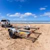 A driver backing up a trailer on a beach.