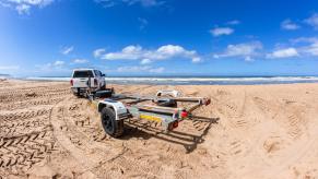 A driver backing up a trailer on a beach.