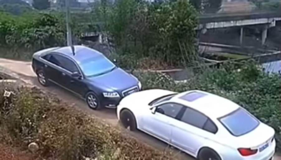 An Audi and a BMW at a narrow two-lane street bridge.