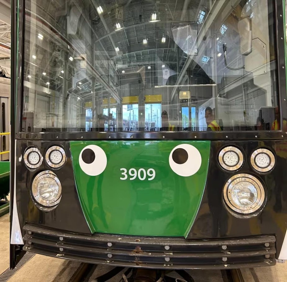 Green Boston light rail train with decorative googly eyes up front.