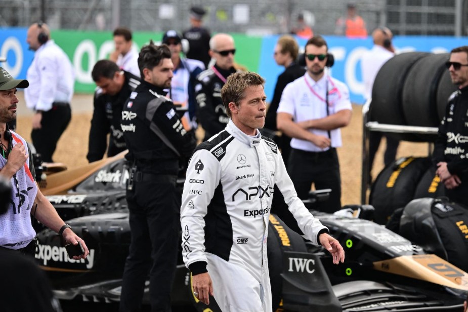 Actor Brad Pitt walks past F1 cars while filming a movie