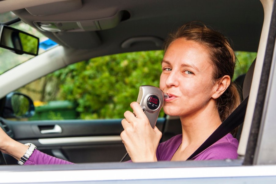 Woman uses a breathalyzer attached to her car.