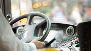 The hands of a driver on the steering wheel of a city bus.