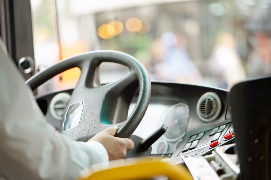 The hands of a driver on the steering wheel of a city bus.