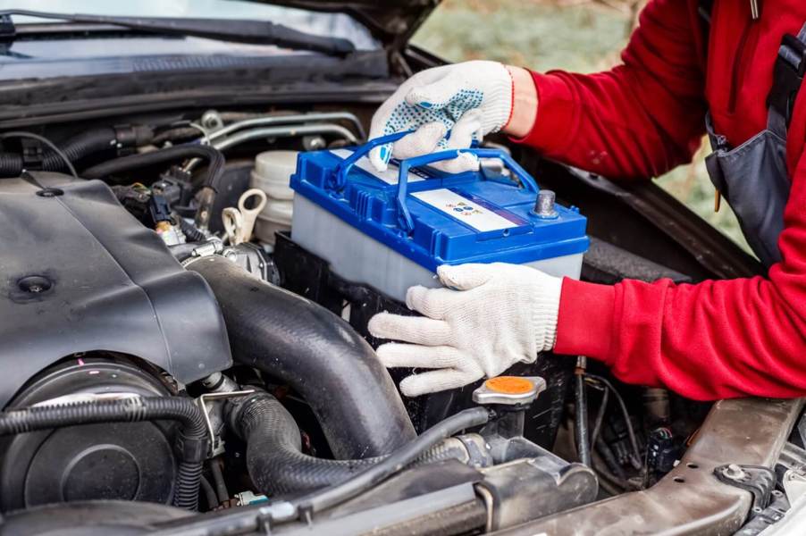 A technician replaces a car battery in an older vehicle.