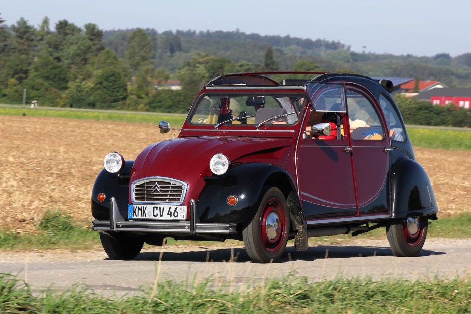 Red and black two-tone Citroën 2CV driving through the countryside.