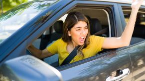 An angry driver gestures out the open window of her car.