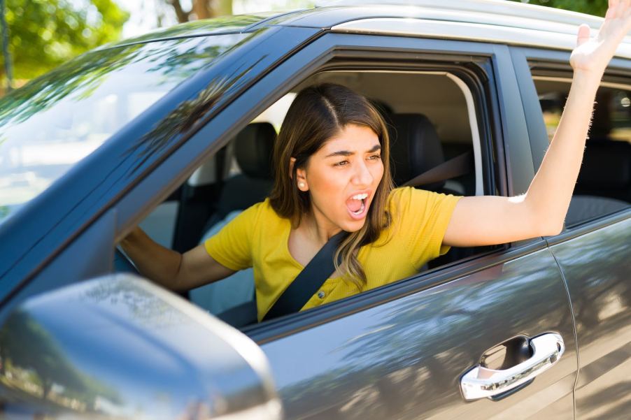 An angry driver gestures out the open window of her car.