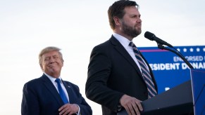 Senator J.D. Vance stands at a podium in Ohio while Presidential candidate Donald Trump smiles behind him