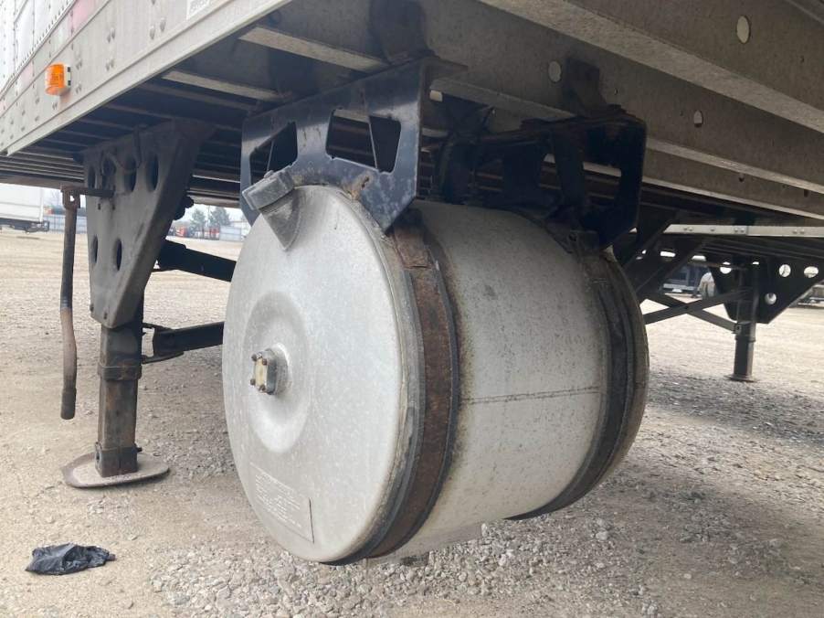 Silver round tank hung beneath a semi truck trailer.