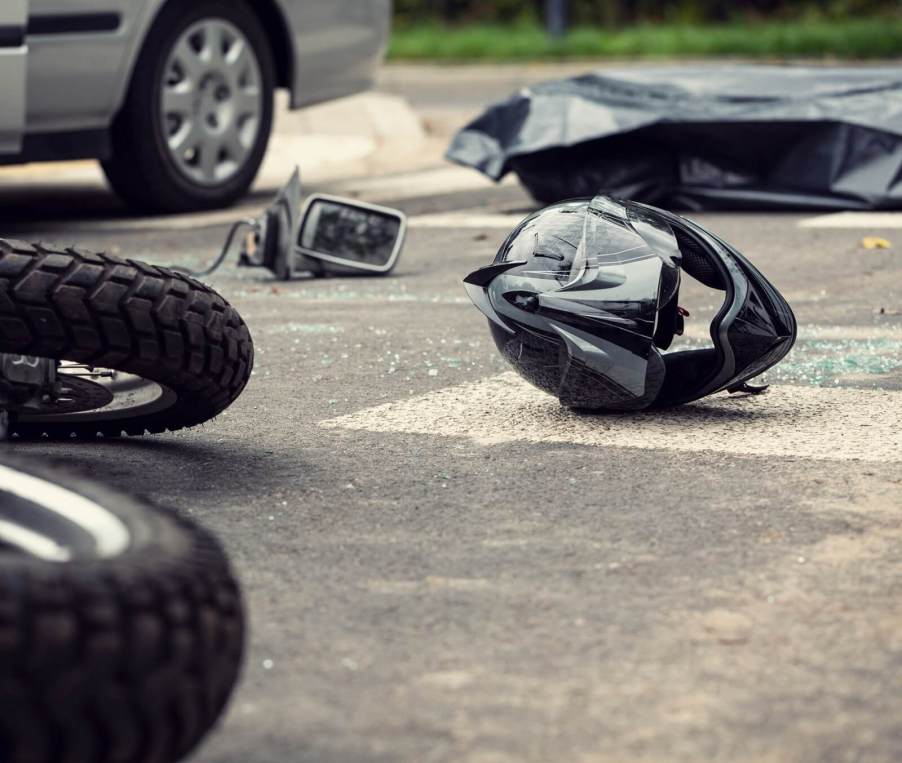 A motorcycle rider and their helmet at the scene of a crash.