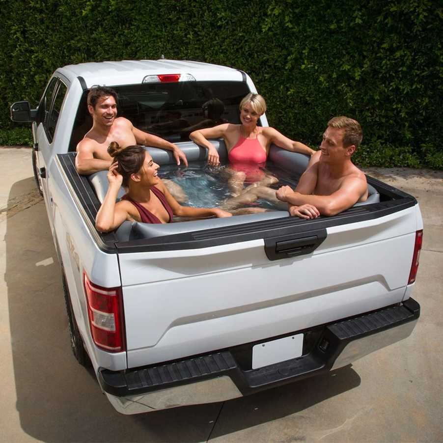 Four people relax in a truck bed filled with water to make a pool.