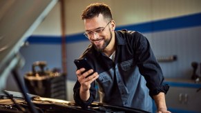 A Millennial mechanic on his phone while in front of a project truck.