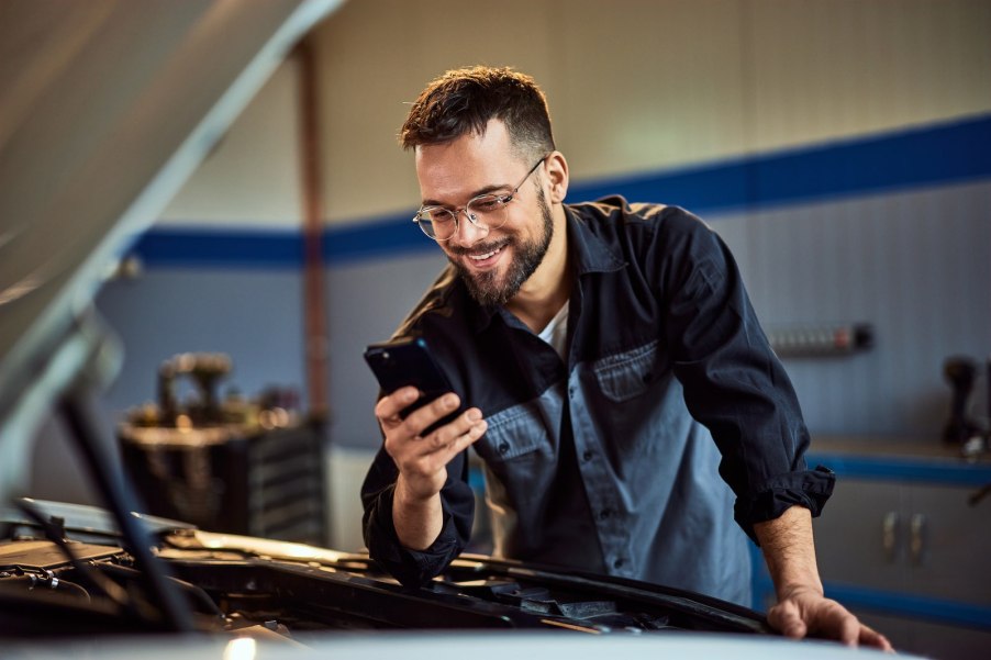 A Millennial mechanic on his phone while in front of a project truck.