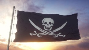 Black flag with a white pirate skull waving in front of a sunset.